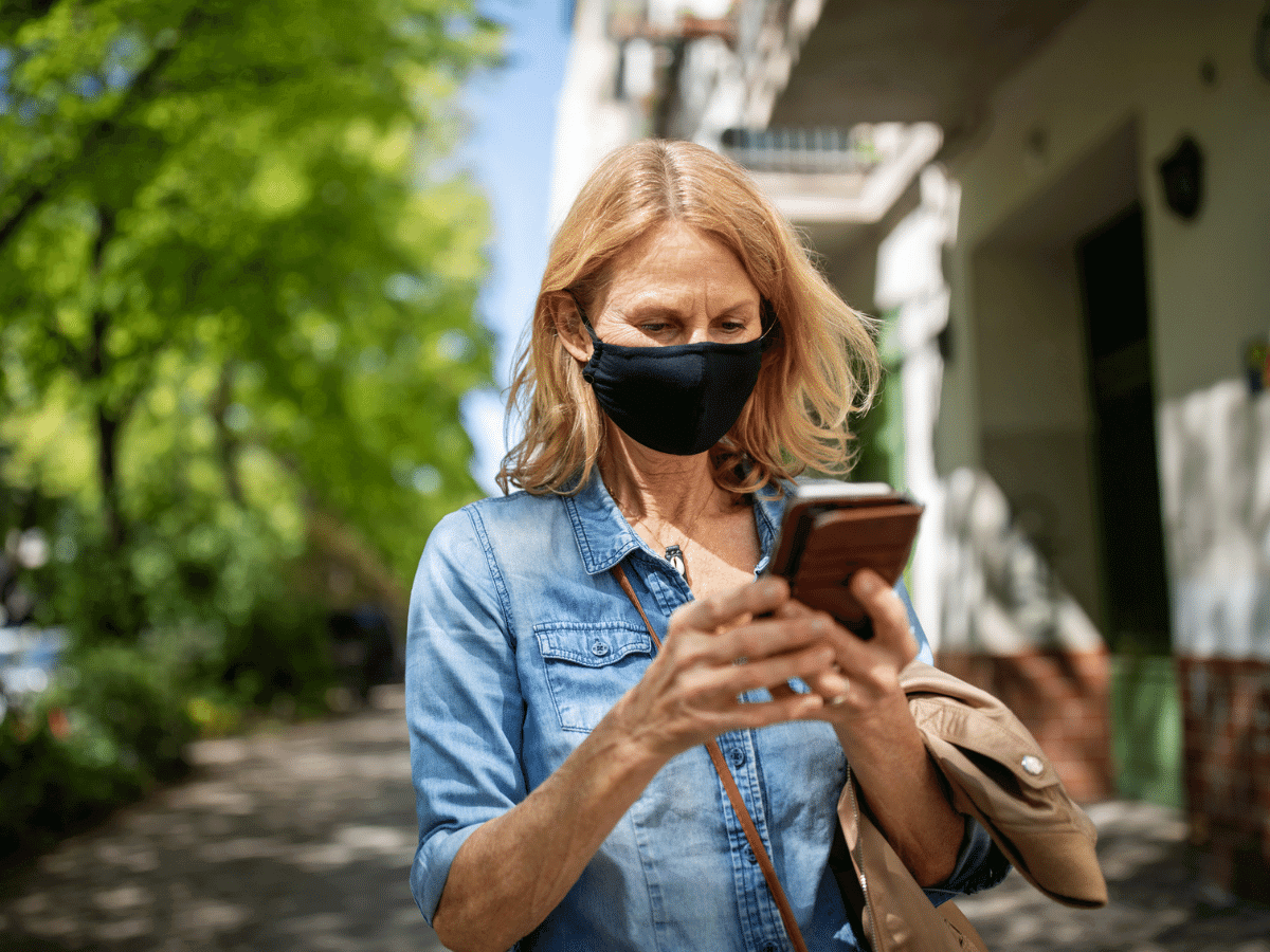 Middle aged woman wearing a mask outside while looking at her smartphone