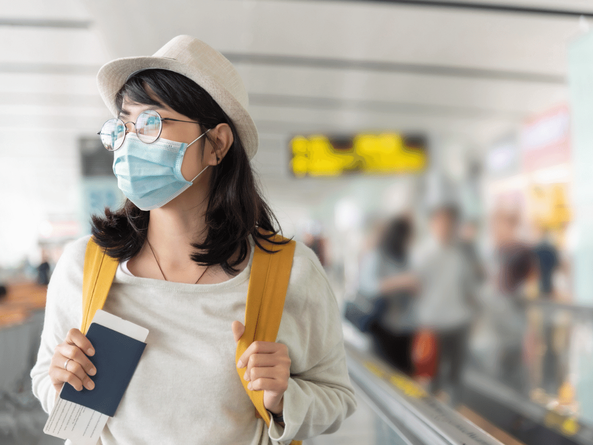 Young woman wearing a mask holding a passport and carrying a backpack at an airport